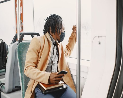 A person looking out the window of a bus during a commute, holding a smartphone but looking away
